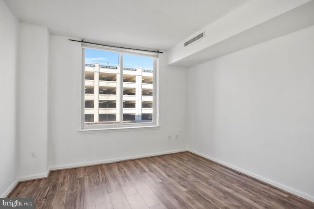 spare room featuring baseboards, a textured ceiling, visible vents, and wood finished floors