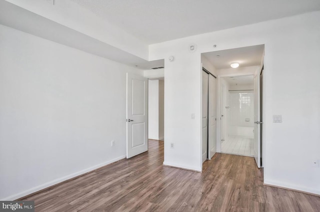 unfurnished bedroom with a closet, wood finished floors, visible vents, and baseboards