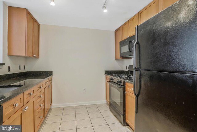 kitchen featuring light tile patterned floors, baseboards, brown cabinets, dark stone counters, and black appliances