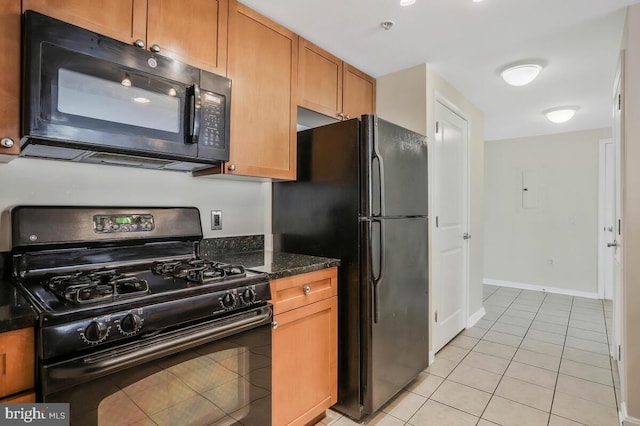 kitchen featuring light tile patterned floors, brown cabinetry, black appliances, dark stone counters, and baseboards