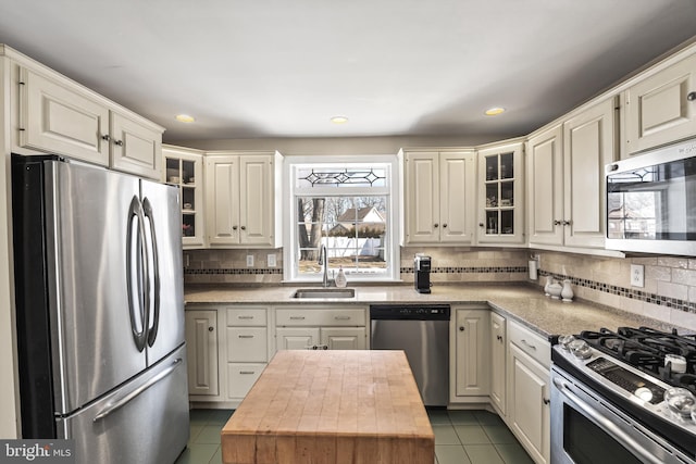 kitchen featuring glass insert cabinets, tile patterned floors, stainless steel appliances, wooden counters, and a sink