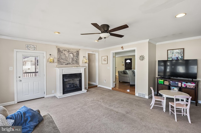 living room featuring baseboards, visible vents, a glass covered fireplace, crown molding, and carpet floors