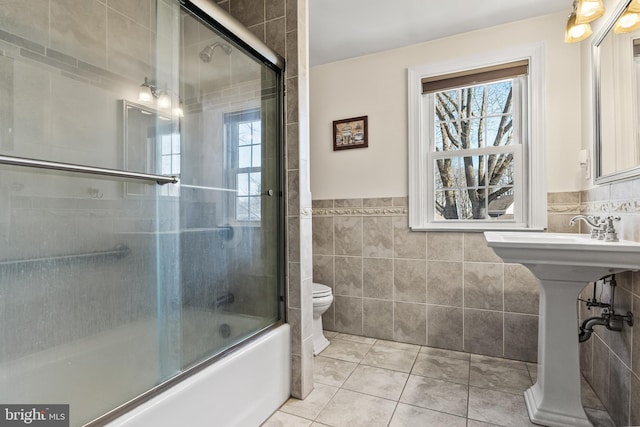 full bath with toilet, a wealth of natural light, tile walls, and tile patterned floors