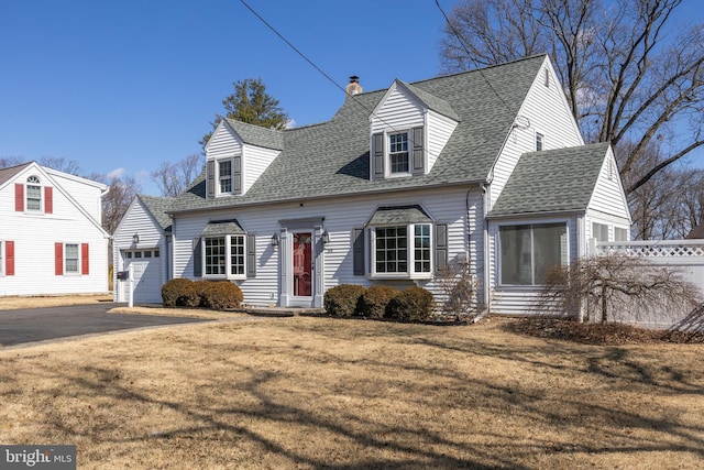 cape cod home with driveway, a shingled roof, and a front yard