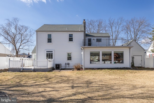 back of house featuring cooling unit, a balcony, fence, a lawn, and a chimney