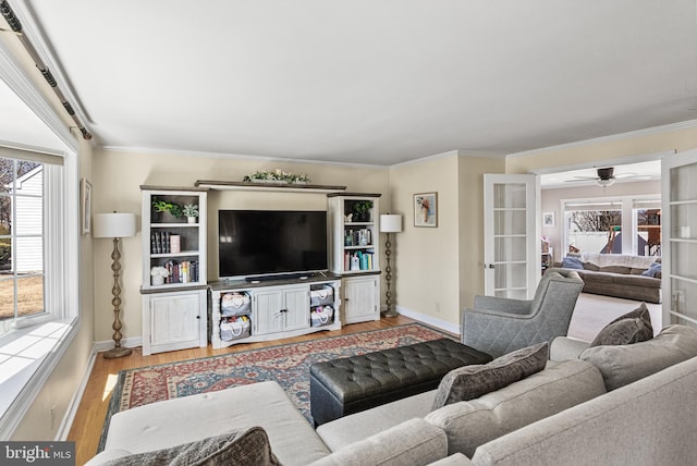 living area with french doors, ornamental molding, a ceiling fan, wood finished floors, and baseboards