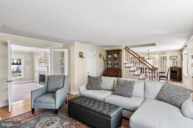 living room featuring a fireplace, crown molding, stairway, wood finished floors, and a chandelier