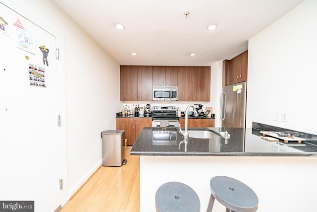 kitchen featuring brown cabinets, appliances with stainless steel finishes, dark stone counters, light wood-type flooring, and a peninsula