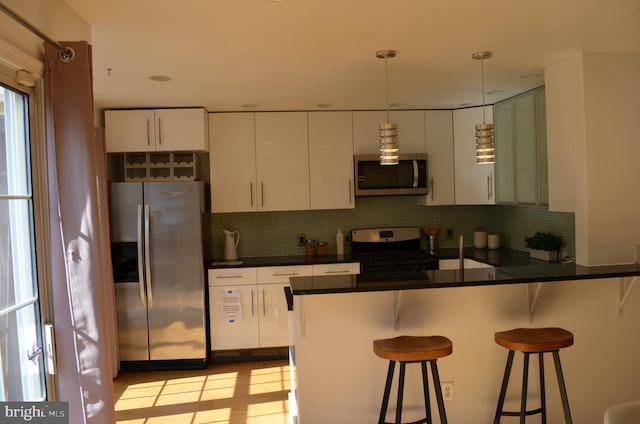 kitchen with stainless steel appliances, a kitchen bar, decorative light fixtures, and white cabinets