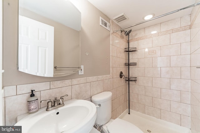 bathroom featuring tile walls, sink, a tile shower, and toilet