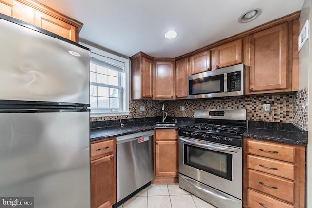 kitchen featuring stainless steel appliances, sink, light tile patterned floors, dark stone counters, and decorative backsplash