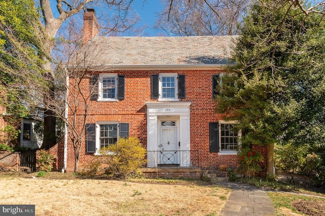 view of front of property with a front lawn, brick siding, and a chimney