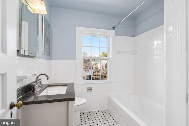 bathroom with toilet, tile walls, wainscoting, tub / shower combination, and vanity