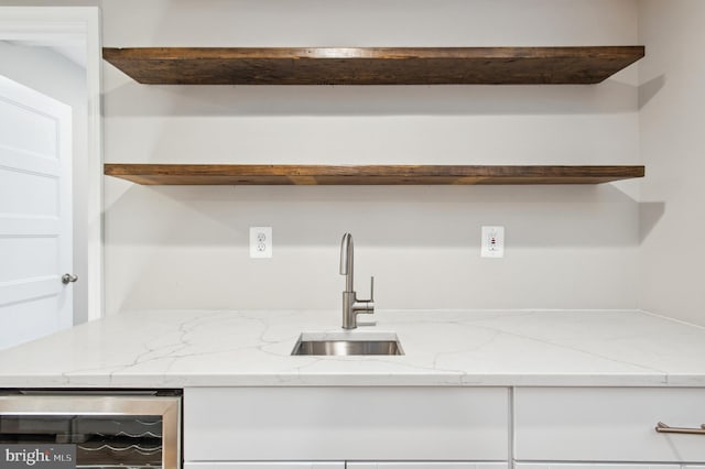 kitchen featuring a sink, wine cooler, light stone countertops, and white cabinetry