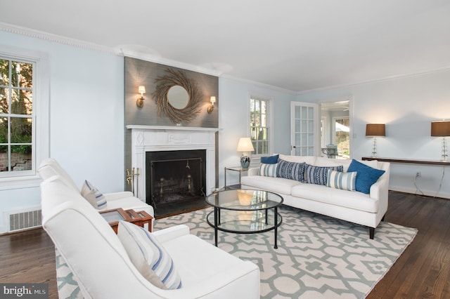 living area featuring a fireplace with flush hearth, crown molding, visible vents, and wood-type flooring