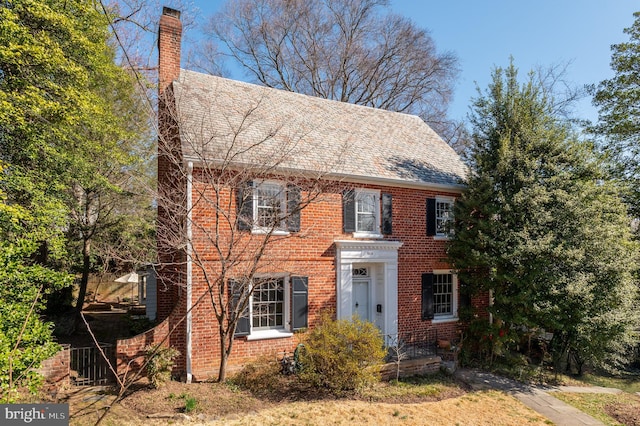 view of front of house with a high end roof, brick siding, and a chimney