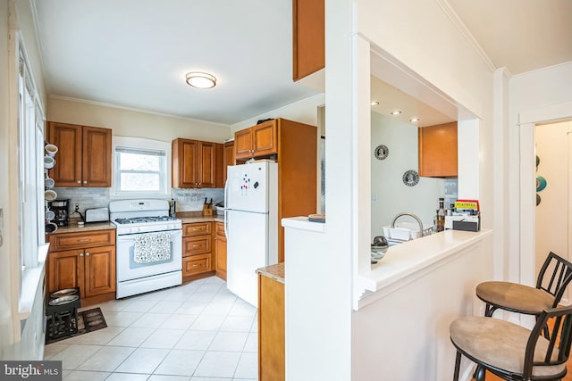 kitchen featuring white appliances, a kitchen breakfast bar, tasteful backsplash, brown cabinetry, and crown molding