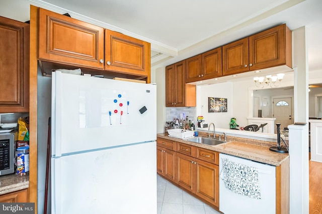 kitchen featuring light tile patterned floors, brown cabinetry, a sink, and freestanding refrigerator