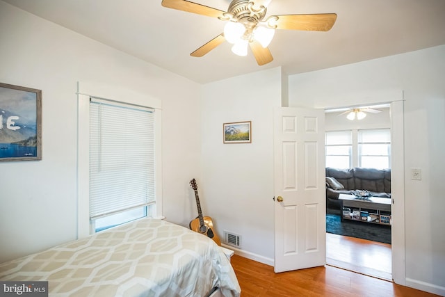 bedroom with ceiling fan, wood finished floors, visible vents, and baseboards