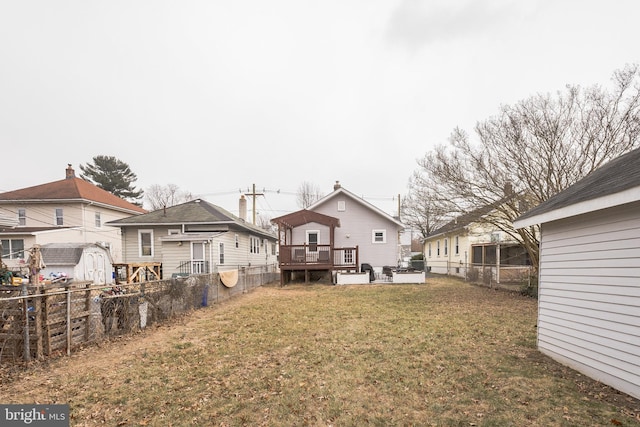 back of property with a lawn, a fenced backyard, an outbuilding, a storage unit, and a deck