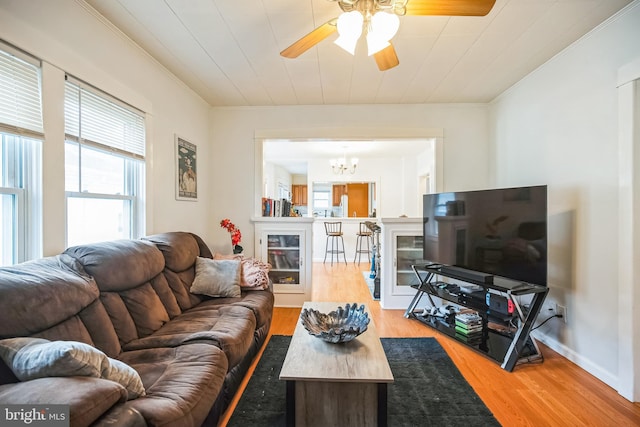 living room featuring ornamental molding, light wood-type flooring, baseboards, and ceiling fan with notable chandelier