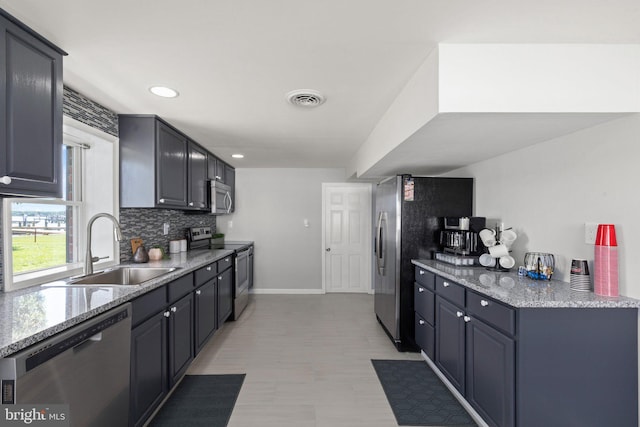 kitchen with appliances with stainless steel finishes, sink, light stone countertops, and decorative backsplash