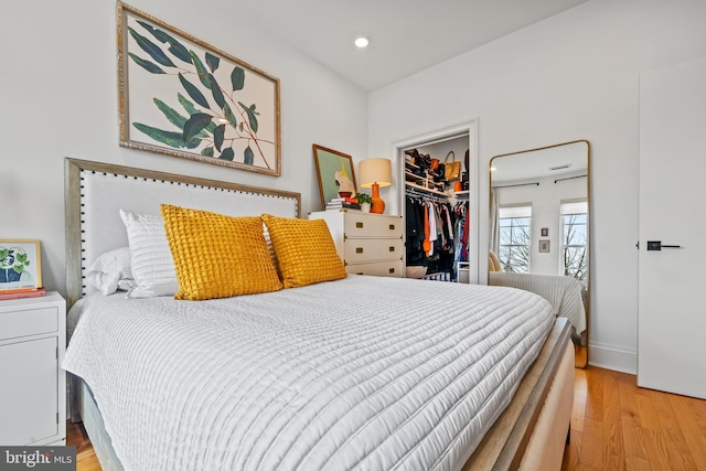 bedroom featuring a walk in closet, recessed lighting, a closet, light wood-style flooring, and baseboards