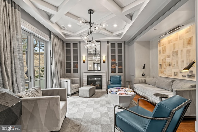 sitting room with a chandelier, coffered ceiling, visible vents, beamed ceiling, and a glass covered fireplace