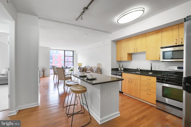 kitchen with light wood finished floors, dark countertops, a breakfast bar area, stainless steel appliances, and light brown cabinetry