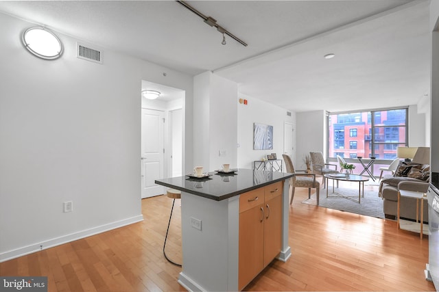 kitchen with dark countertops, visible vents, light wood-style floors, a wall of windows, and a kitchen breakfast bar