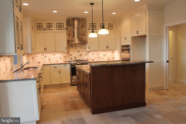 kitchen with stainless steel appliances, a center island, white cabinets, dark stone countertops, and wall chimney range hood