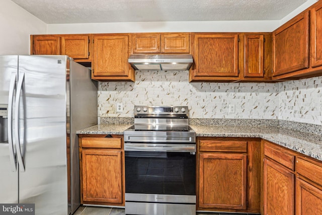 kitchen featuring light stone countertops, under cabinet range hood, tasteful backsplash, and appliances with stainless steel finishes