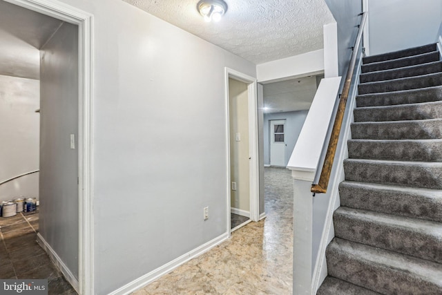 stairway featuring baseboards and a textured ceiling