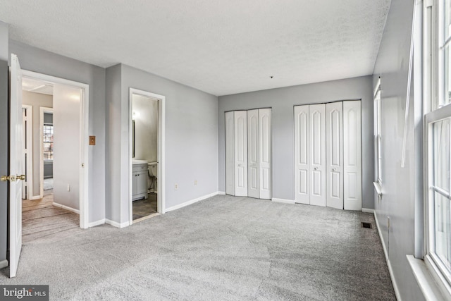 unfurnished bedroom with visible vents, baseboards, a textured ceiling, carpet floors, and two closets