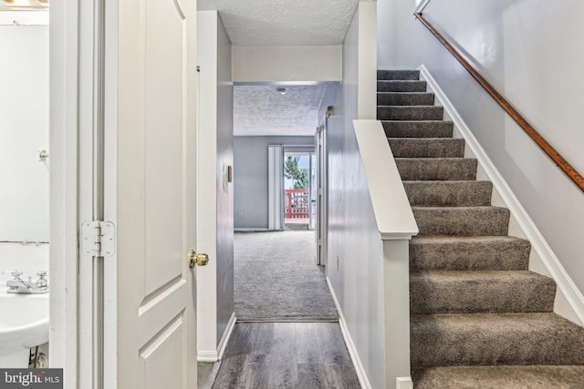 stairway featuring baseboards, a textured ceiling, and wood finished floors