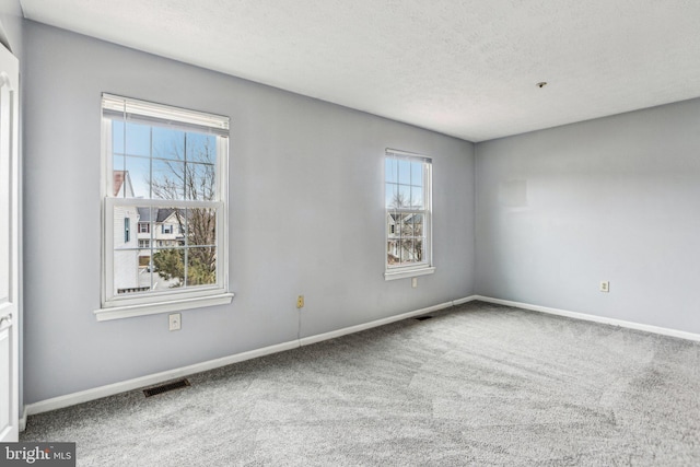 carpeted empty room with visible vents, a textured ceiling, and baseboards