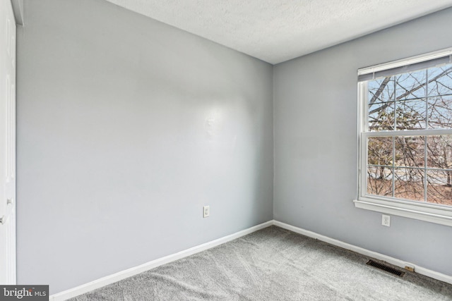 spare room featuring carpet floors, baseboards, visible vents, and a textured ceiling