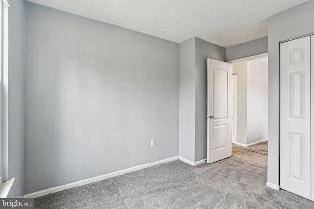 unfurnished bedroom with light colored carpet, a textured ceiling, and baseboards