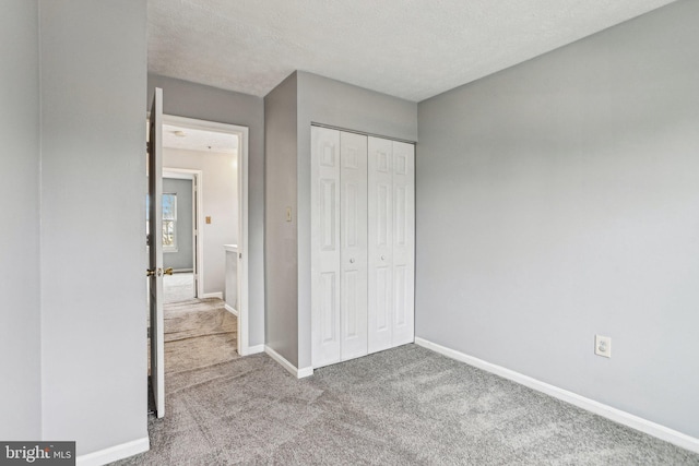 unfurnished bedroom with carpet, a closet, a textured ceiling, and baseboards