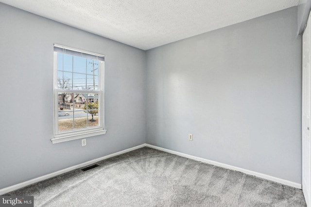 carpeted spare room featuring visible vents, baseboards, and a textured ceiling