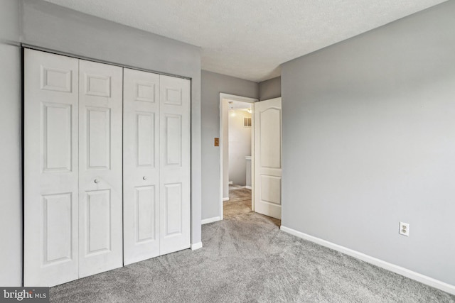 unfurnished bedroom with a closet, light colored carpet, a textured ceiling, and baseboards