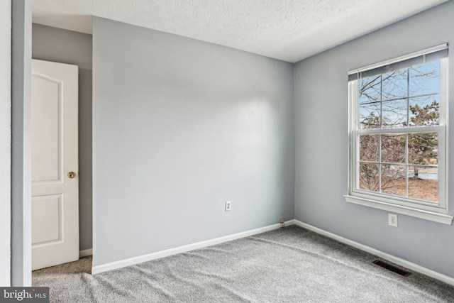 spare room featuring light carpet, a textured ceiling, visible vents, and baseboards