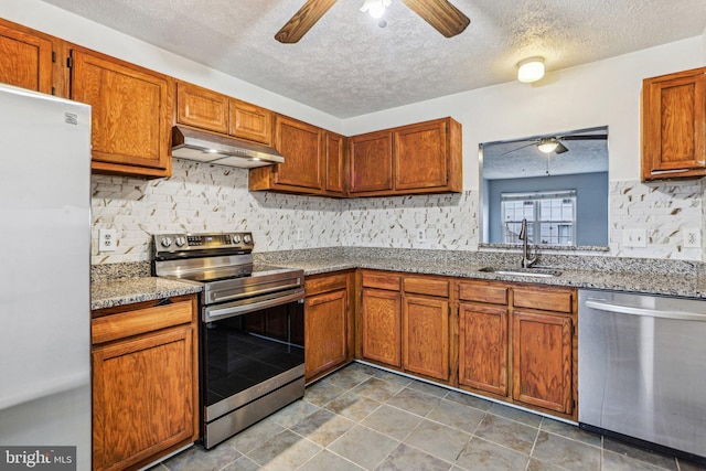 kitchen featuring under cabinet range hood, appliances with stainless steel finishes, brown cabinetry, and a ceiling fan