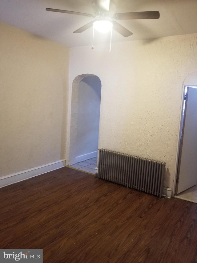 empty room with arched walkways, radiator heating unit, and wood finished floors