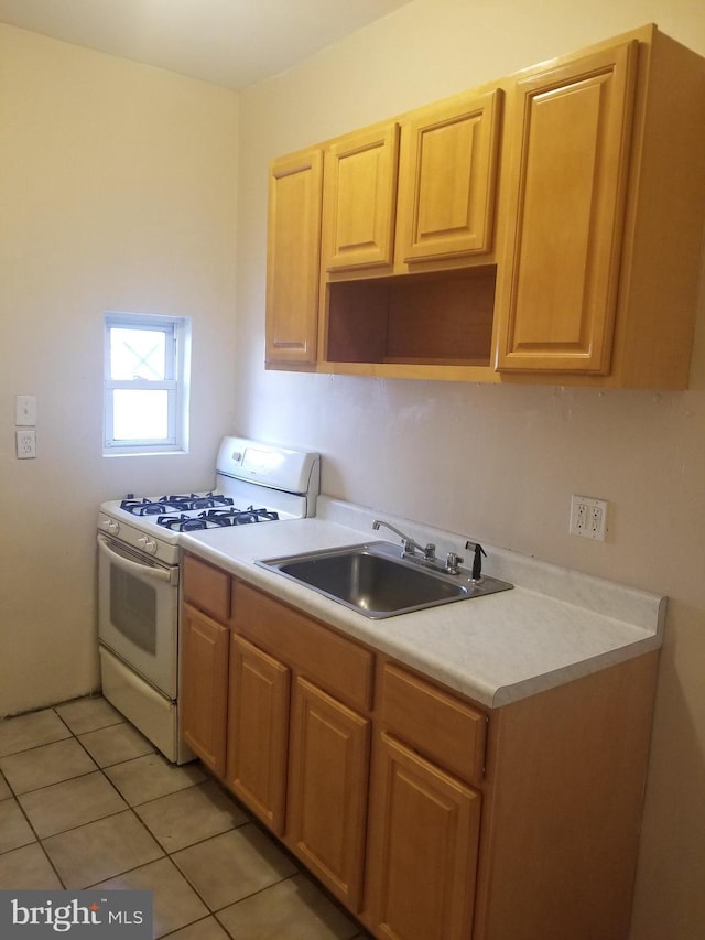 kitchen with light tile patterned floors, light countertops, light brown cabinets, a sink, and white range with gas stovetop