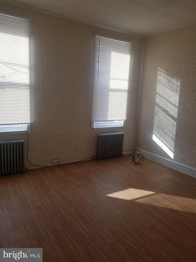 spare room with a textured wall, radiator heating unit, and wood finished floors