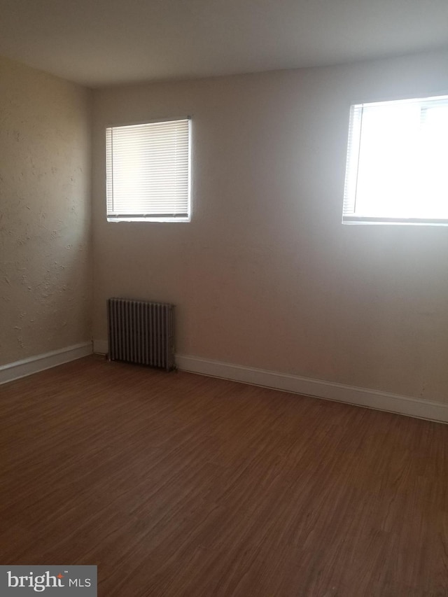 spare room featuring baseboards, radiator heating unit, and wood finished floors