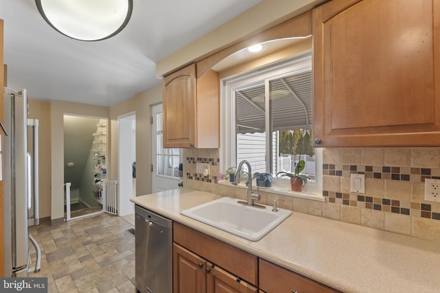 kitchen featuring a sink, light countertops, appliances with stainless steel finishes, stone finish flooring, and tasteful backsplash