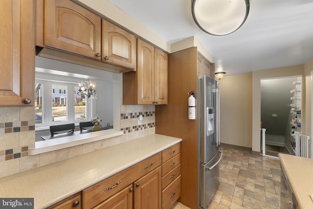 kitchen featuring tasteful backsplash, baseboards, stainless steel fridge with ice dispenser, light countertops, and stone tile flooring