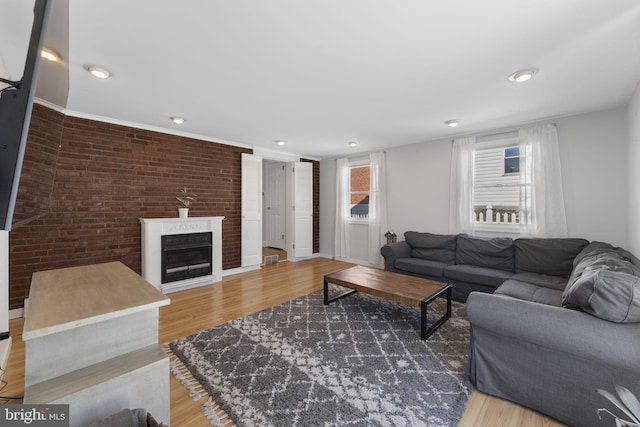 living room featuring a glass covered fireplace, recessed lighting, brick wall, and wood finished floors